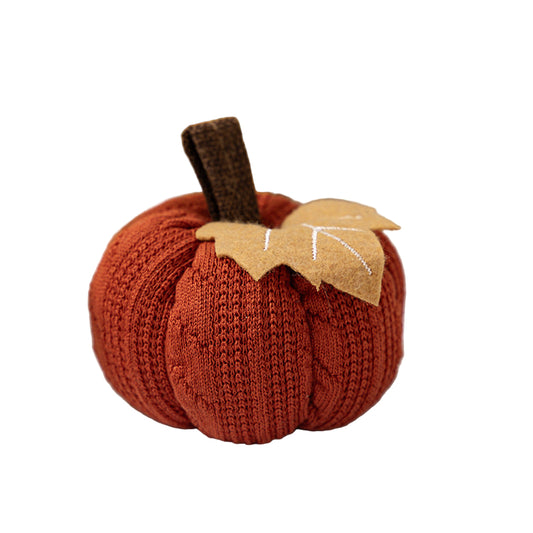 Knitted pumpkin decoration with a leaf on a white surface, with pumpkins in the background.