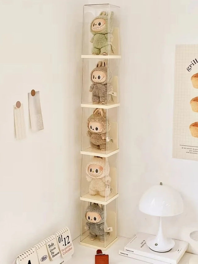 Tall clear storage tower with small plush toys on a shelf against a white wall.