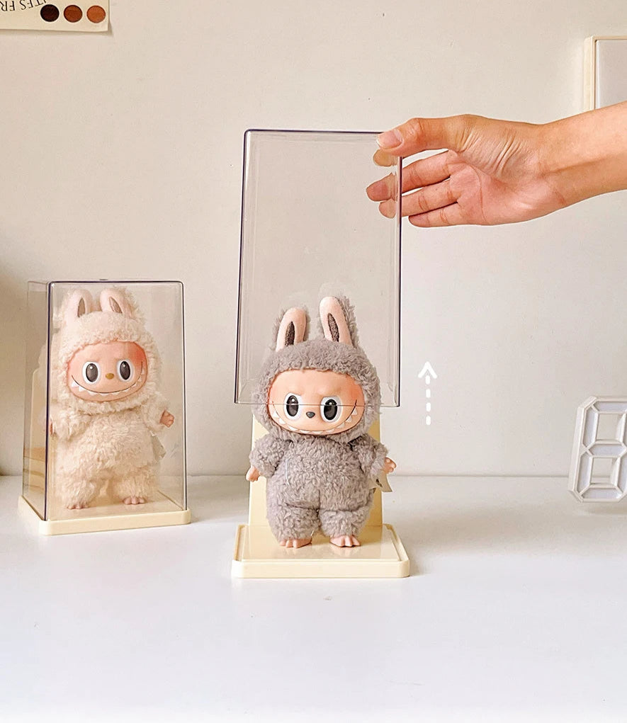 Plush toy with bunny ears being held by a hand on a white surface.