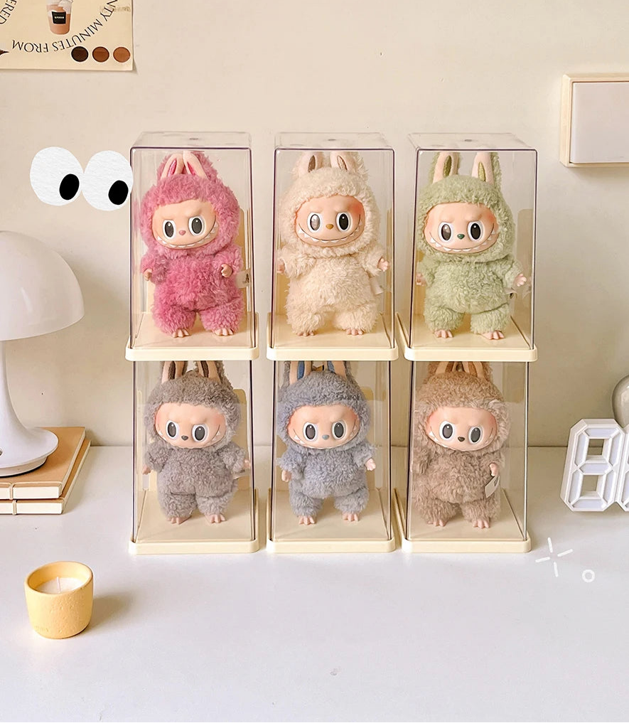 Six small plush toys in clear boxes on a light surface with a neutral background