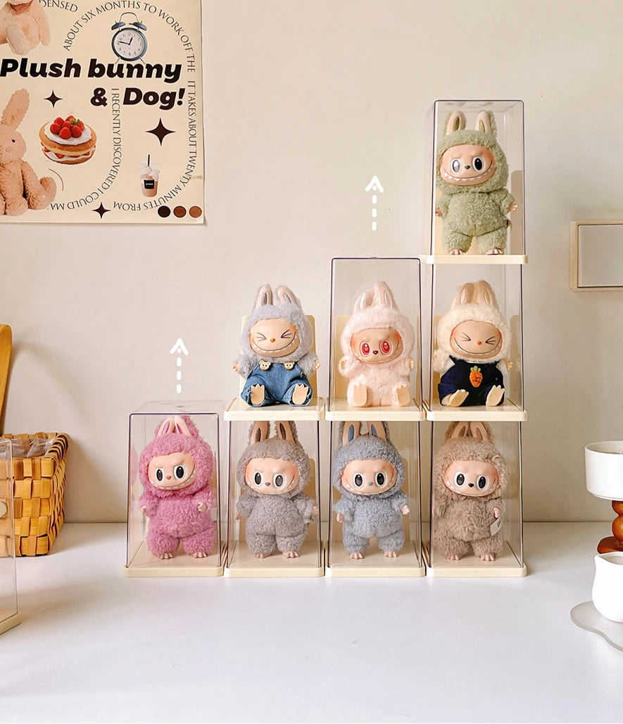 Plush toys in clear display cases on a white surface with a poster in the background.