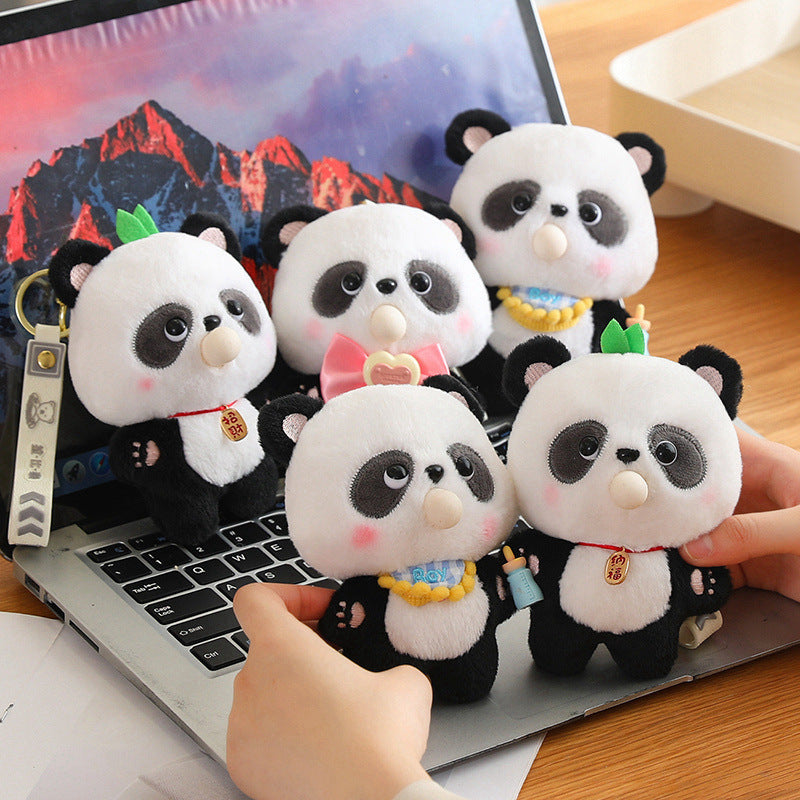 Plush panda keychains held in front of a laptop on a wooden desk