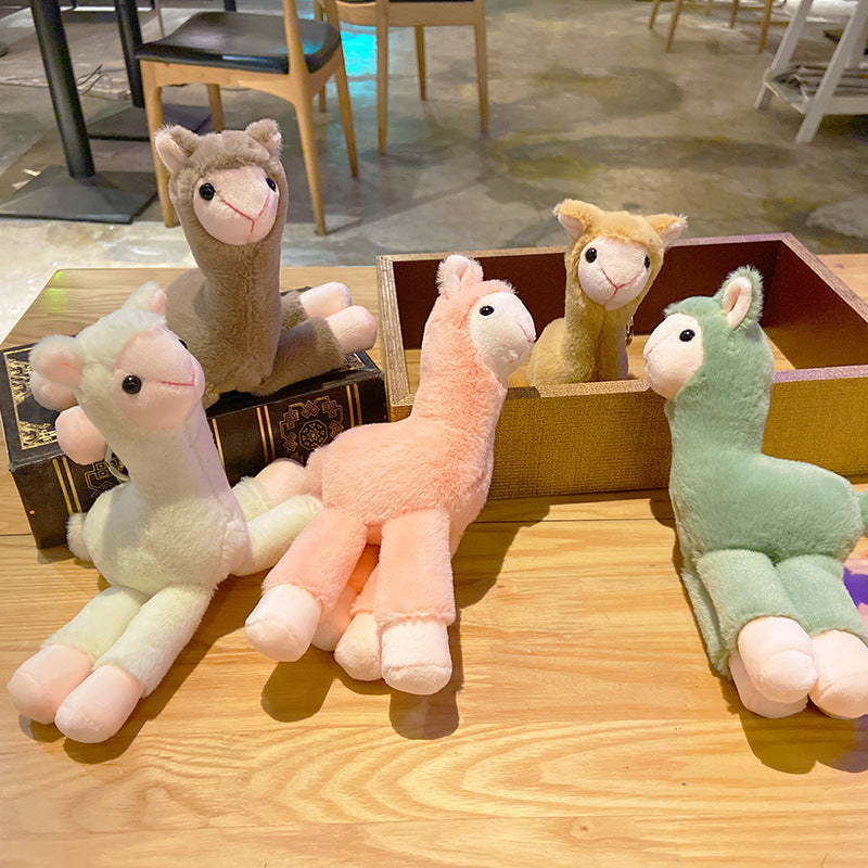 Four plush alpaca toys in different colors on a wooden table.
