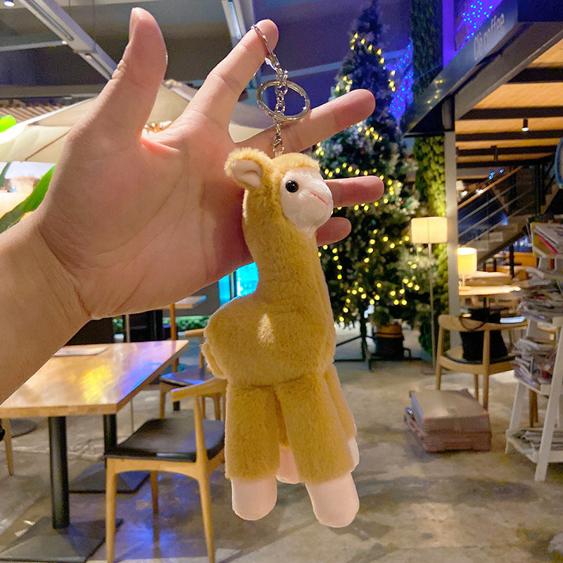 Hand holding a plush llama keychain with a blurred indoor background