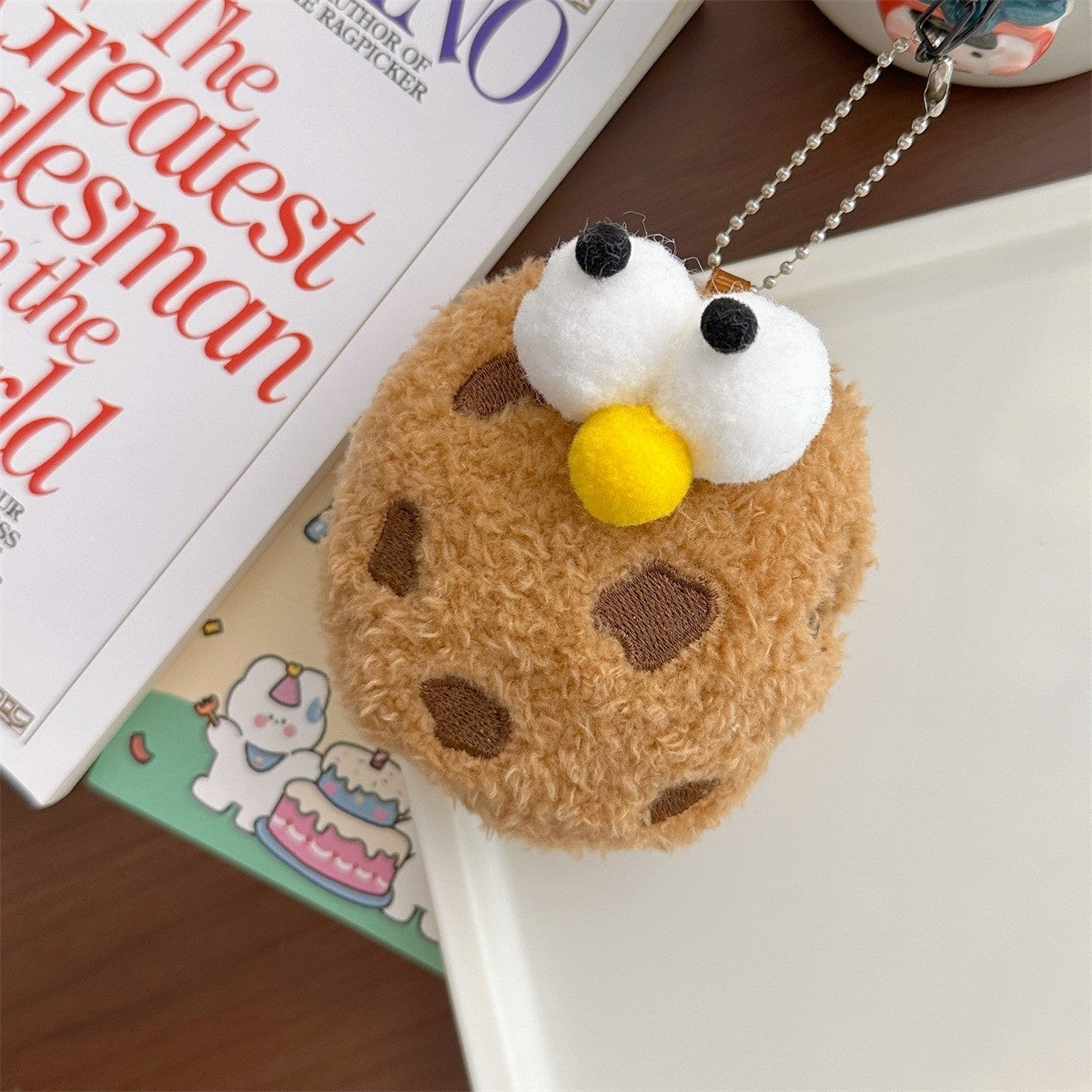 Plush keychain resembling a cookie with a book in the background