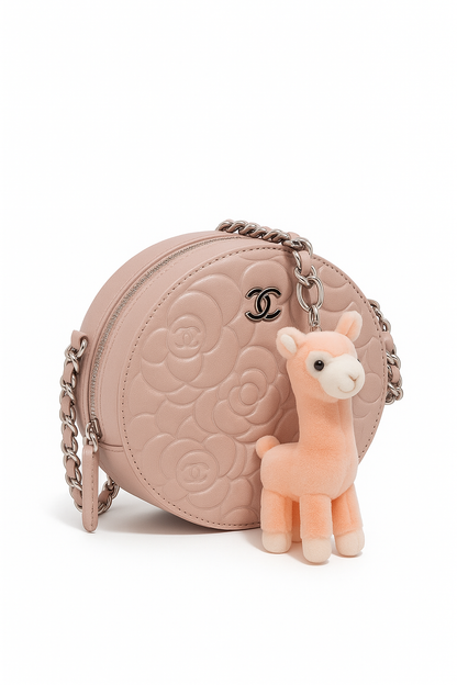 Pink quilted handbag with a small plush llama toy on a white background