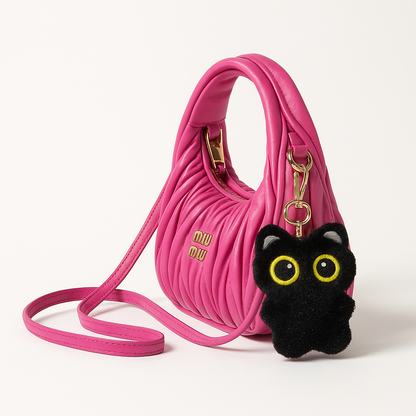 Pink handbag with a black cat-shaped keychain on a white background