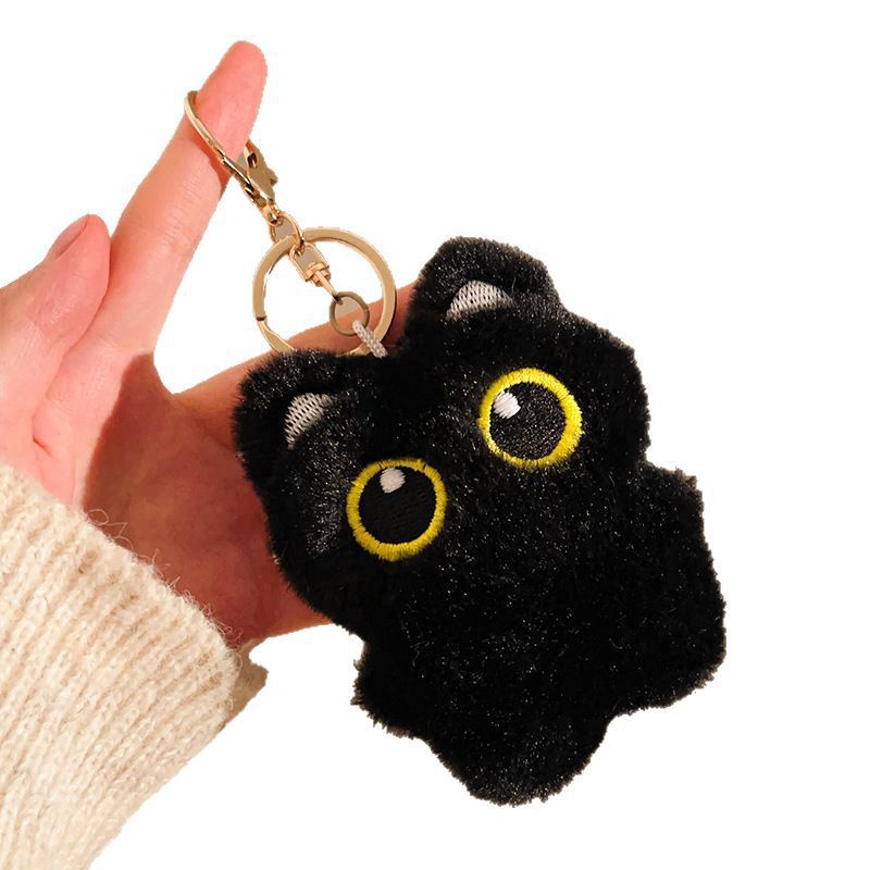 Black plush keychain with yellow eyes held by a hand against a white background