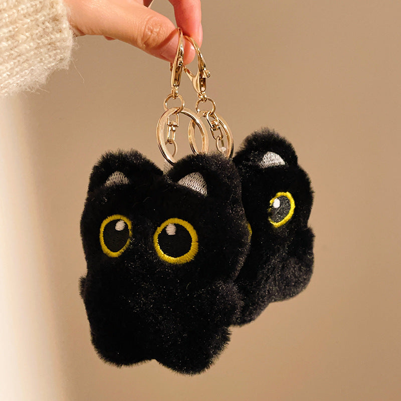 Black fluffy keychain shaped like a cat with yellow eyes on a beige background