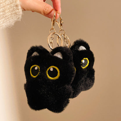 Black fluffy keychain shaped like a cat with yellow eyes on a beige background
