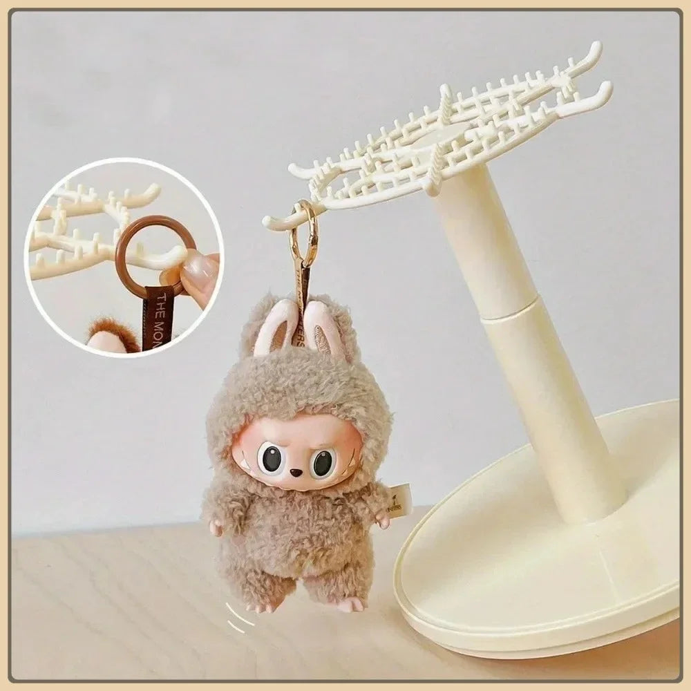 Plush keychain with a small face on a stand with a close-up inset showing the brand name.