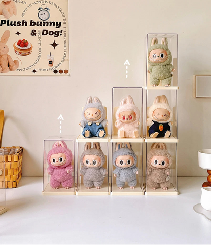 Plush toys in clear display cases on a white surface with a poster in the background.