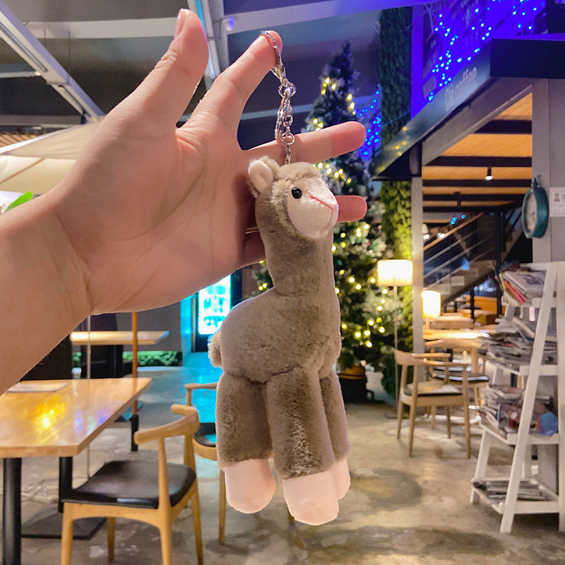 Plush llama keychain held in front of a restaurant interior with Christmas decorations.
