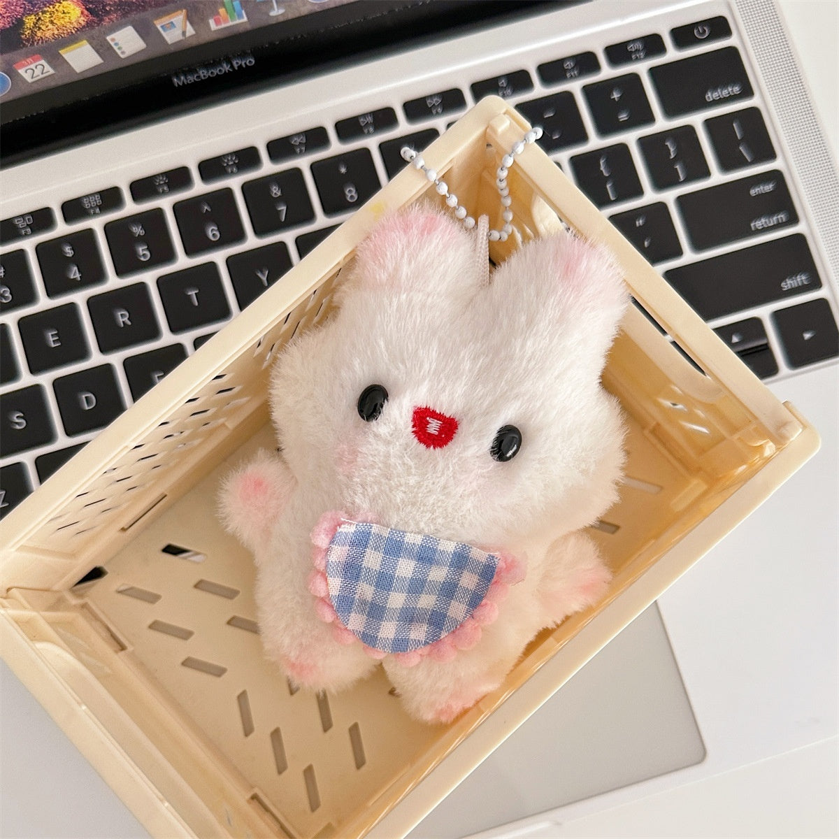 White plush bunny keychain with a blue checkered dress in a wooden basket on a laptop keyboard.