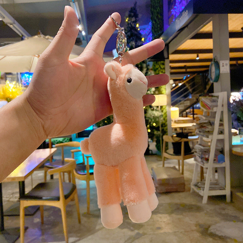 Plush llama keychain held by a hand in an indoor setting with tables and chairs.